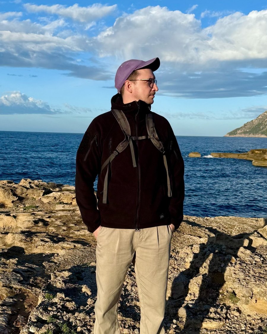 Mario Müller in a cap and dark jacket standing on a rocky coast by the sea